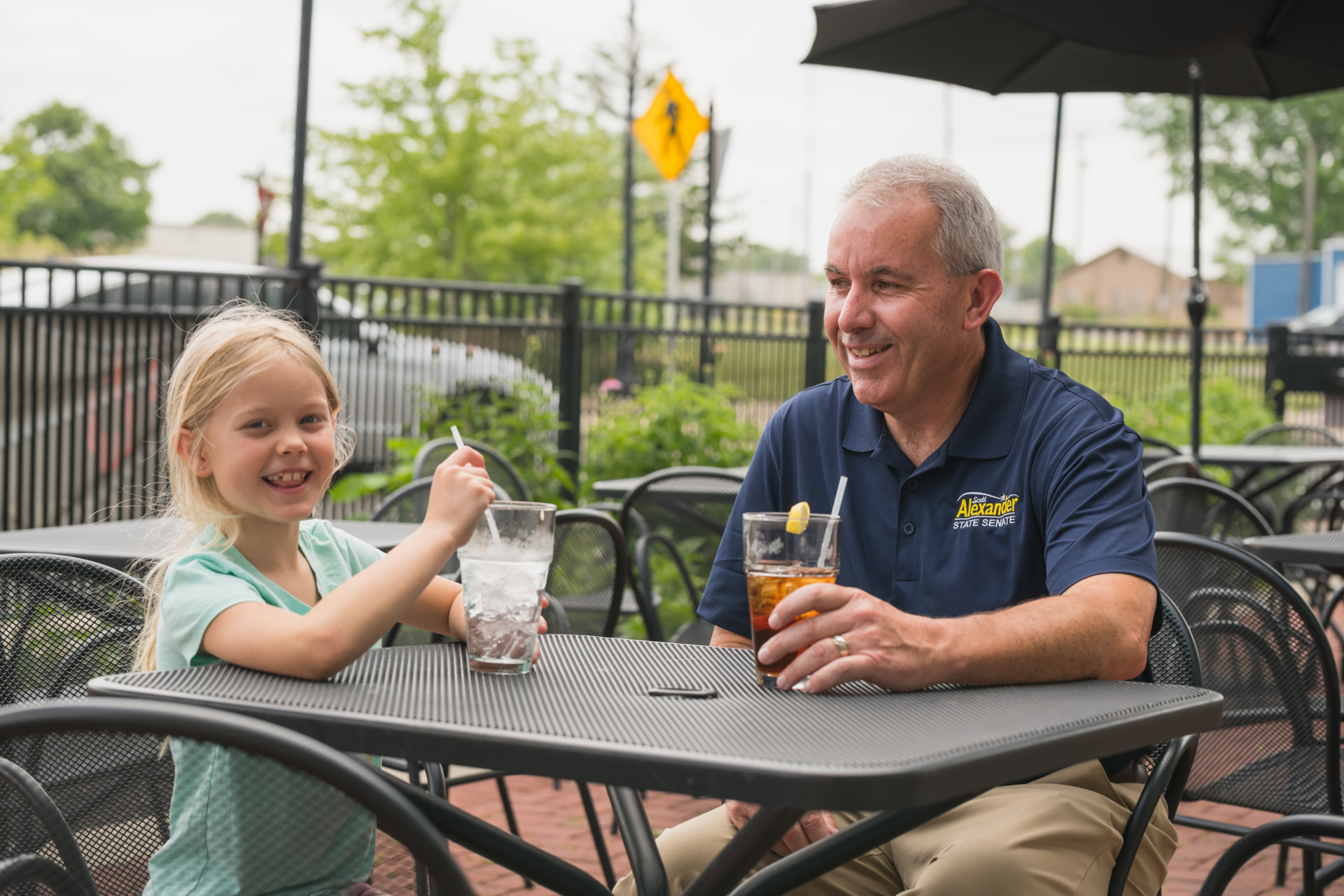 Scott Alexander talking with a young girl at an outdoor patio table.